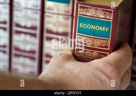 Eine Hand, die nach einem Buch mit dem Titel Wirtschaft, Konzept der Wissenschaft und ökonomischer Wissenserwerb greift Stockfoto