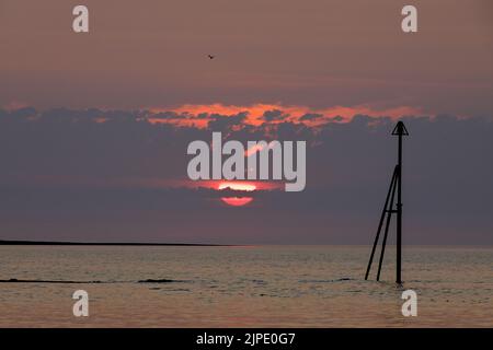 Eine untergehende Sonne, die durch die Wolken über den Horizont hinaus ins Meer spähe. Stockfoto