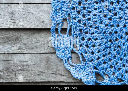 Blauer Teppich mit Figuren von Herzen für den Boden, handgehäkelt, auf einem grauen Holzhintergrund. Ecke einer Tischdecke auf dem Boden eines Holzzimmers platziert Stockfoto