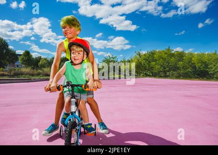 Zwei Brüder zusammen Portrait, großer Junge schieben kleines Fahrrad Stockfoto