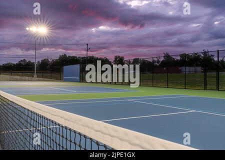 Abendliches Foto von oben auf einem Tennisplatz Netz auf einem Outdoor blauen Tennisplätze mit hellblauen Pickleball Linien mit Court Lichter eingeschaltet. Stockfoto