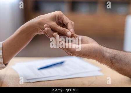 Die Hand einer erwachsenen kaukasischen Frau gibt ihrem Ex-Mann am Tisch einen Ring mit Scheidungspapieren, Nahaufnahme, abgeschnitten Stockfoto