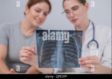 Der Arzt konsultiert eine kaukasische Frau und kommentiert die Röntgenaufnahme der Lunge. Stockfoto