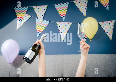 Hände einer Frau mit einer Flasche und einem Glas Champagner liegen auf dem Bett im Schlafzimmer mit Ballons und Girlande geschmückt.Zeit für sich selbst celebratio Stockfoto