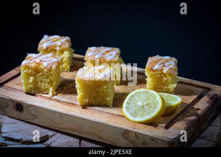 Leckere Zitronen-Nieselkuchen und frische Zitronenscheiben auf Holzbrett Stockfoto