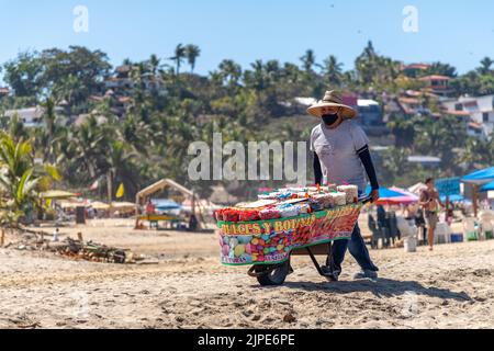 Ein Mann, der einen Wagen schiebt, der Süßigkeiten und Snacks an einem Strand in Sayulita, Mexiko verkauft Stockfoto