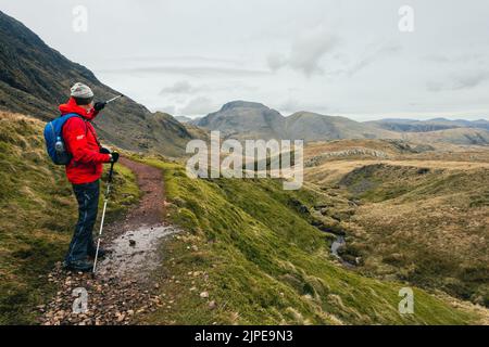 Wanderer genießen die Aussicht und zeigen in Richtung Great Gable und Green Gable unter Great End, Lake District National Park, Cumbria, UK Landschaften Stockfoto