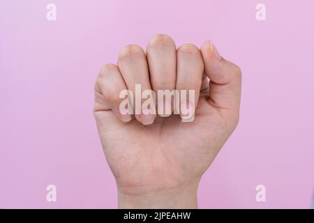 Hand einer lateinischen Frau, die ihre Nägel in einer geschlossenen Handpose zeigt, im Hintergrund ein rosa Karton, halb angeordnete Nägel bereit für die Realisierung eines Stockfoto