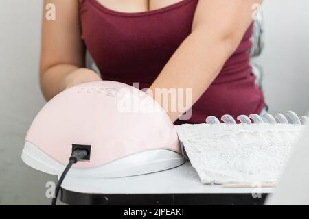 Nahaufnahme einer 48 Watt rosa LED-Nagellampe für semi permanente Acryl-Gel. Frau bekommen eine Maniküre für die persönliche Nagelpflege. Konzept der Schönheit und Eitelkeit Stockfoto