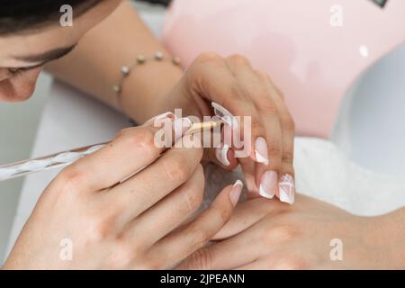 latina Manikurist Herstellung von Polygel Nägel, mit dem Pinsel, um das Gel durch den Nagel zu verbreiten. Frau vorsichtig die spezielle Flüssigkeit, um die g zu Formen Stockfoto