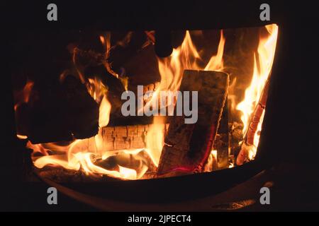 Nahaufnahme von Holzstücken, die in einem Eisenofen brennen, zum Kochen für die traditionelle ländliche Küche Stockfoto