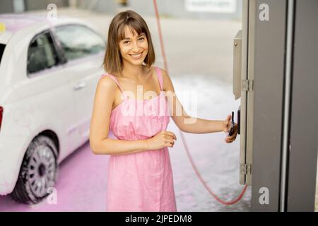 Frau, die bei der Autowäsche kontaktlos mit dem Smartphone bezahlt Stockfoto