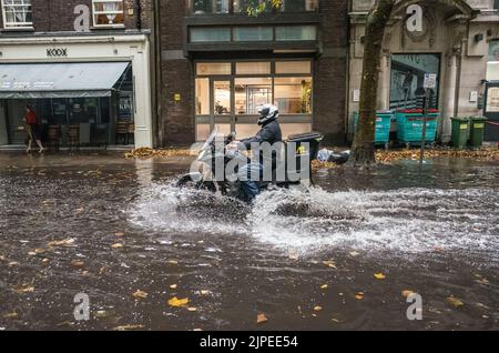 Fahrradkurier fährt durch überflutete Straße nach Sturm in Central London, England, Großbritannien. Stockfoto
