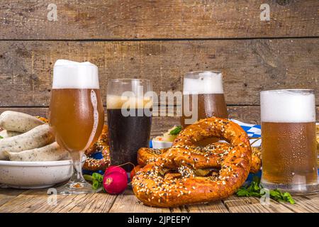 Oktoberfest-Food-Hintergrund, traditionelle bayerische Festtagsmenüs, Würstchen mit Brezeln, Sauerkraut, Bierglas und Tassen auf sonnenbeleuchtetem Holzbac Stockfoto