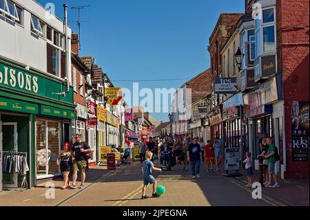 Menschenmassen auf der High Street, die liebevoll als „Chip Pan Allee“ in Skegness bekannt ist, mit einem Kind, das Ball spielt Stockfoto