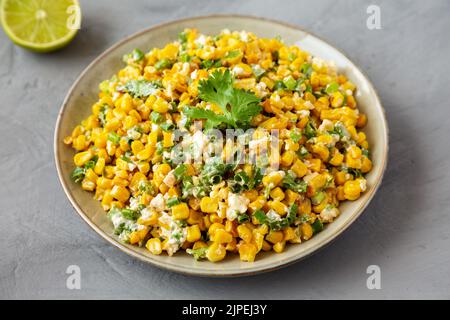 Hausgemachte mexikanische Street Corn Esquites auf einem Teller auf grauem Hintergrund, Seitenansicht. Stockfoto