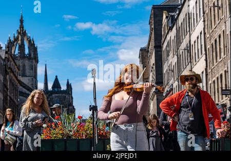 Royal Mile, Edinburgh, Schottland, Großbritannien, 17.. August 2022. Darsteller auf der Royal Mile im Sonnenschein. Bild: Credit: MEG LaGrande spielt auf der Straße Geige oder Geige, während die Leute vorbeigehen. Sally Anderson/Alamy Live News Stockfoto