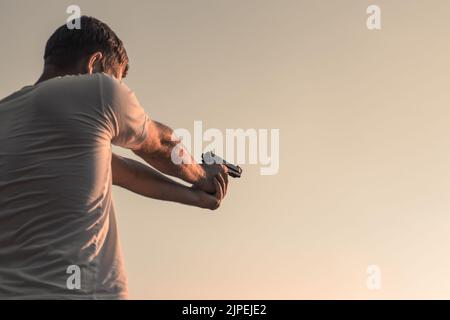 Ein Mann mit einem Gewehr in den Händen zielt darauf ab. Schießen auf der Straße, Verbrechen. Kopierraum. Stockfoto