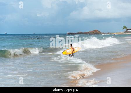 Ein Surfer, der gegen den blauen Himmel und weiße Wolken ins Meer eindringt. Salvador, Brasilien. Stockfoto