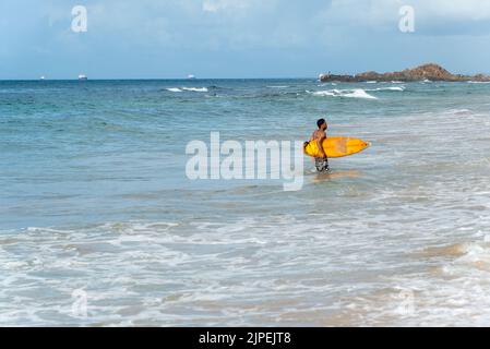 Ein Surfer, der gegen den blauen Himmel und weiße Wolken ins Meer eindringt. Salvador, Brasilien. Stockfoto