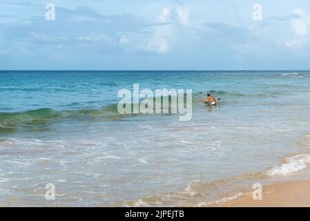 Ein Surfer, der gegen den blauen Himmel und weiße Wolken ins Meer eindringt. Salvador, Brasilien. Stockfoto