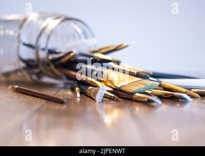 Eine selektive Fokusaufnahme von Farbbürsten, die aus einem Glasgefäß auf eine Holzoberfläche fallen Stockfoto