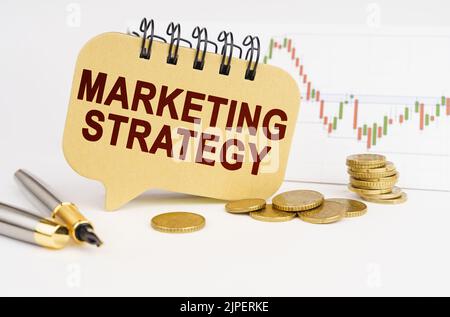 Geschäftskonzept. Auf dem Tisch sind Münzen, ein Stift, eine Grafik und ein Schild mit der Aufschrift - MARKETINGSTRATEGIE Stockfoto