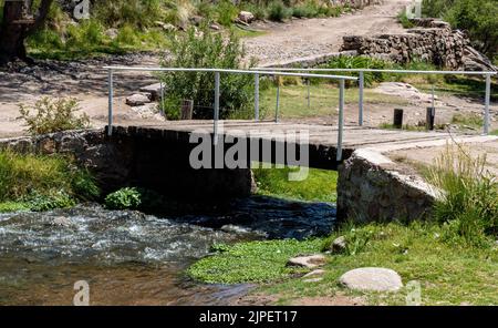 Die Aussicht auf eine kleine Holzbrücke, die an einem sonnigen Tag über den Fluss führt Stockfoto