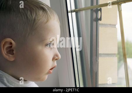 Ein kleiner Junge sitzt und schaut aus dem Fenster. Nahaufnahme Stockfoto