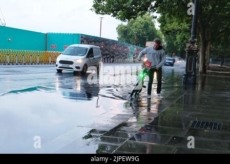 London, Großbritannien. 17.. August 2022. Ein Radfahrer läuft mit seinem Fahrrad durch Oberflächenregenwasser entlang des Victoria Embankment, nachdem schwere Regenschauer die Hauptstadt getroffen hatten, was in Teilen der Stadt zu lokalen Überschwemmungen führte, da die Abflüsse schwer zu bewältigen waren. Kredit: Elfte Stunde Fotografie/Alamy Live Nachrichten Stockfoto