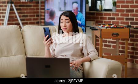 Frau, die mit dem Manager während einer digitalen Videokonferenz auf dem Smartphone arbeitet. Junge Erwachsene asiatische Person winkt an Telefonkamera, während Remote-Arbeit und Teilnahme an Videoclip mit Kollegen. Stockfoto
