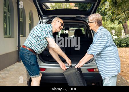 Ältere Leute, die im Sommer Taschen in den Kofferraum legen, um sie auf eine Reise in den Ruhestand zu verlassen. Reisen auf der Straße zur Erholung, Packen Gepäck und Koffer für Städtereise Urlaub. Stockfoto