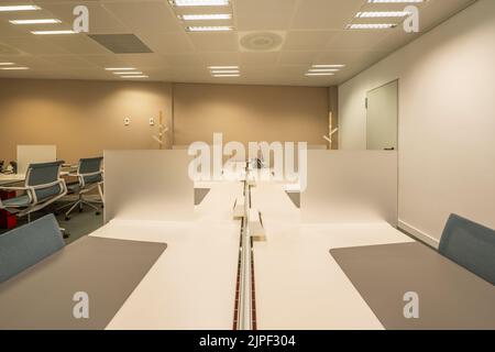 Kabinen im Coworking-Büro mit Tischteilern, Kabelschienen, Teppichböden, technischen Decken und weißen Drehstühlen Stockfoto