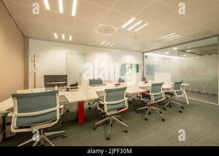 Kabinen im Coworking-Büro mit Tischteilern und weißen Drehstühlen Stockfoto