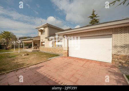 Weißes Aluminium-Tür einer Garage in Stein und weißem Backstein Einfamilienhaus Stockfoto