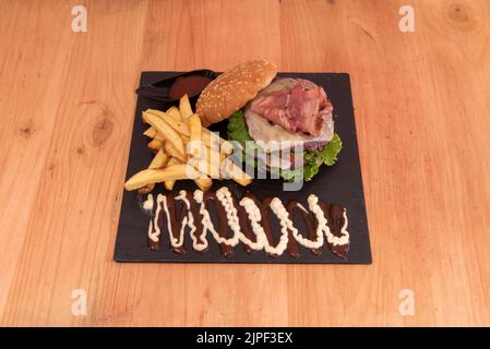 Köstlicher Double Beef Burger mit geschmolzenem Käse, gebratenem Speck, Salat und Tomaten, Saucen und hausgemachten Pommes frites Stockfoto