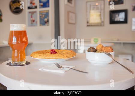 Einige spanische Tapas von Kartoffel-Omelett mit Füllung, Kroketten verschiedener Geschmacksrichtungen und bewölktes Bier mit Schaum Stockfoto