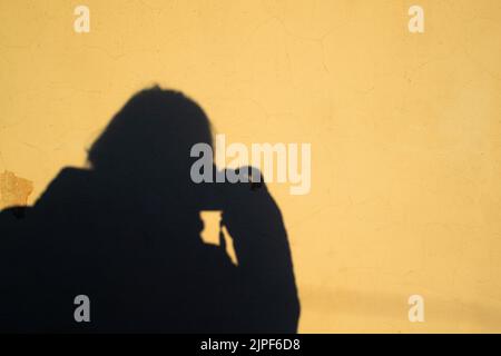 Selfie einer Fotografin in Form eines menschlichen Schattens mit einer Kamera auf einem gelben alten schäbigen Wandhintergrund. Speicherplatz kopieren. Stockfoto