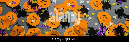 Banner mit Halloween Hintergrund: Glänzendes Konfetti in Form von orangefarbenen Kürbissen, schwarzen Spinnen und lila, goldenen Sternen. Stockfoto