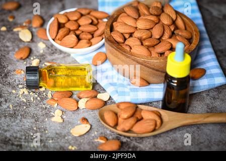 Mandelöl und Mandelnüsse auf Schale dunkler Hintergrund, leckeres süßes Mandelöl in Glasflasche, geröstete Mandelnuss für gesunde Lebensmittel und Snack Organi Stockfoto