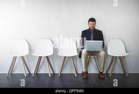 Die beste Zeit, um sich vor dem Interview vorzubereiten. Studioaufnahme eines Geschäftsmannes, der vor weißem Hintergrund in einer Schlange wartet. Stockfoto