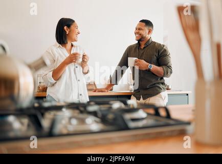Liebevolles Paar, das Kaffee trinkt und redet, sich verbindet und Spaß hat, während es zu Hause Zeit miteinander verbringt. Lächelnd, verliebt und sorglos umarmt sich das Paar Stockfoto