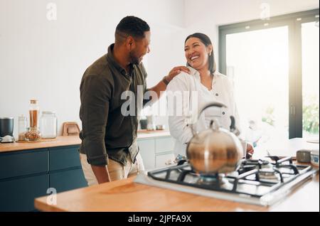 Fröhliches und liebevolles Paar, das sich verbindet und Spaß hat, während man Zeit zusammen in der Küche verbringt. Lächelnd, verliebt und unbeschwert Paar lachen, teilen ein Stockfoto