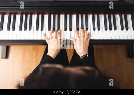 Draufsicht auf Frauenhände, die beim Lesen von Notenblättern Klavier spielen. Stockfoto