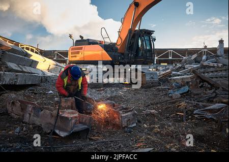 Ein Mitarbeiter im Helm schneidet alte Metallbalken für das Recycling vor Ort Stockfoto