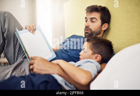 Es war einmal ein schöner Prinz... ein junger Mann, der mit seinem Sohn zu Hause ein Buch las. Stockfoto