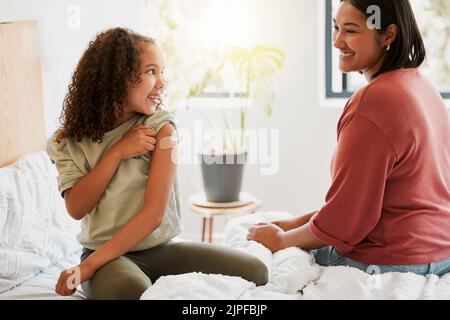 Mädchen mit Covid-Impfstoff zeigt Mutter geimpften Arm mit Gips als covid19 Schutz für ein Kind in einem Schlafzimmer zu Hause. Kind nach einer Injektion Stockfoto