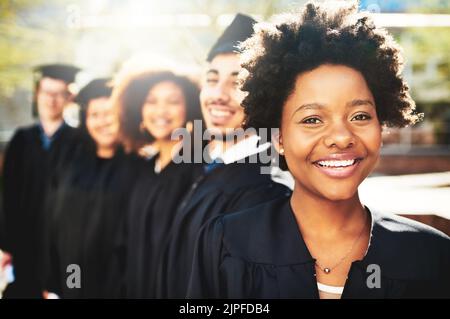 Mein Erfolg beginnt hier. Porträt eines lächelnden Studenten am Abschlusstag mit Mitschülern im Hintergrund. Stockfoto