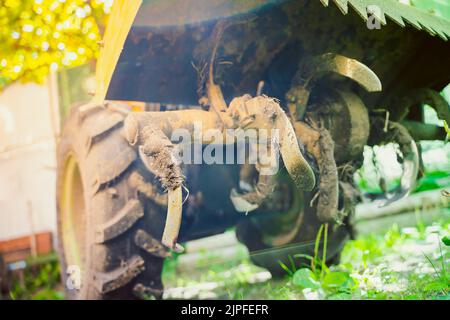 Aktiver Motoblock-Schneider im Schlamm aus der Nähe, Ansicht von unten. Kleiner Traktor zum Pflügen eines Gemüsegartens in der Landwirtschaft Stockfoto