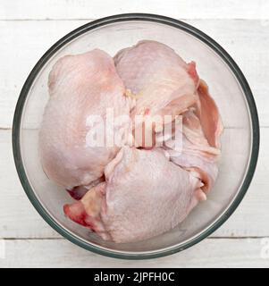 Draufsicht auf Hähnchenschenkel in Glasschale auf Holzhintergrund Stockfoto